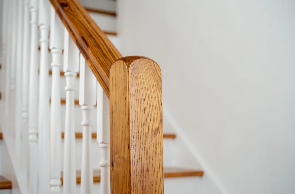Détail de la rampe et du poteau d'escalier en bois rénové avec finition huilée et barreaux blancs